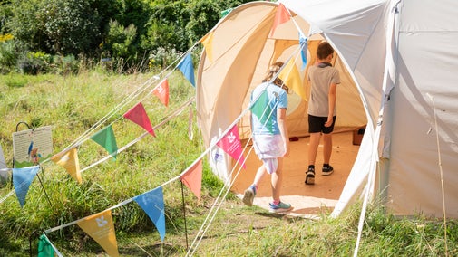 Two children walk into a play tent which has bunting